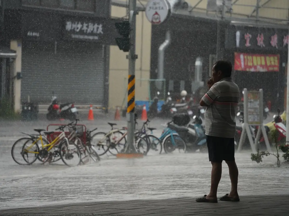 高雄街道在豪雨中積水，行人站在騎樓邊觀察雨勢