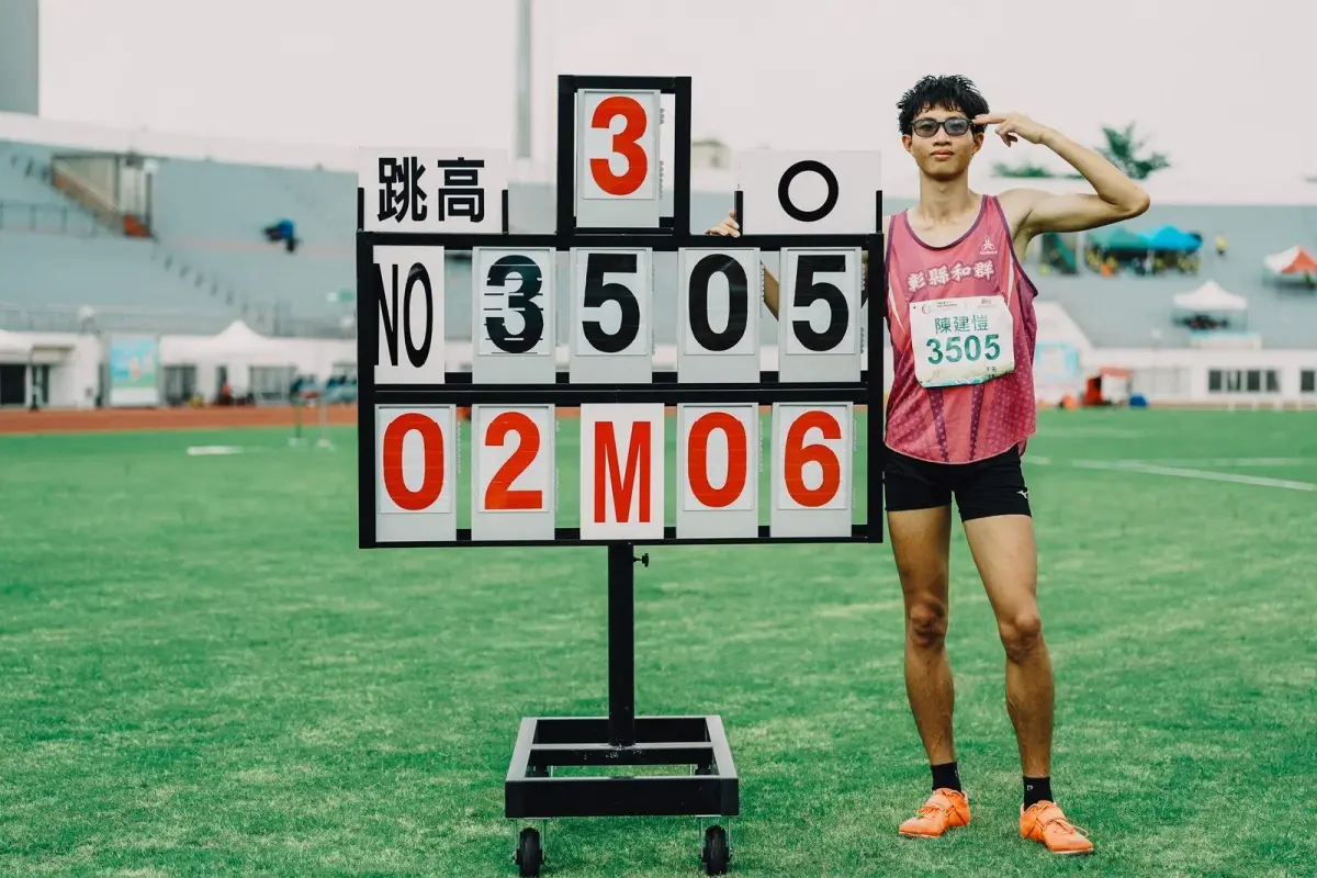台灣少年跳高選手在田徑場上以背越式動作越過橫桿，後方可見落墊與模糊的觀眾席。