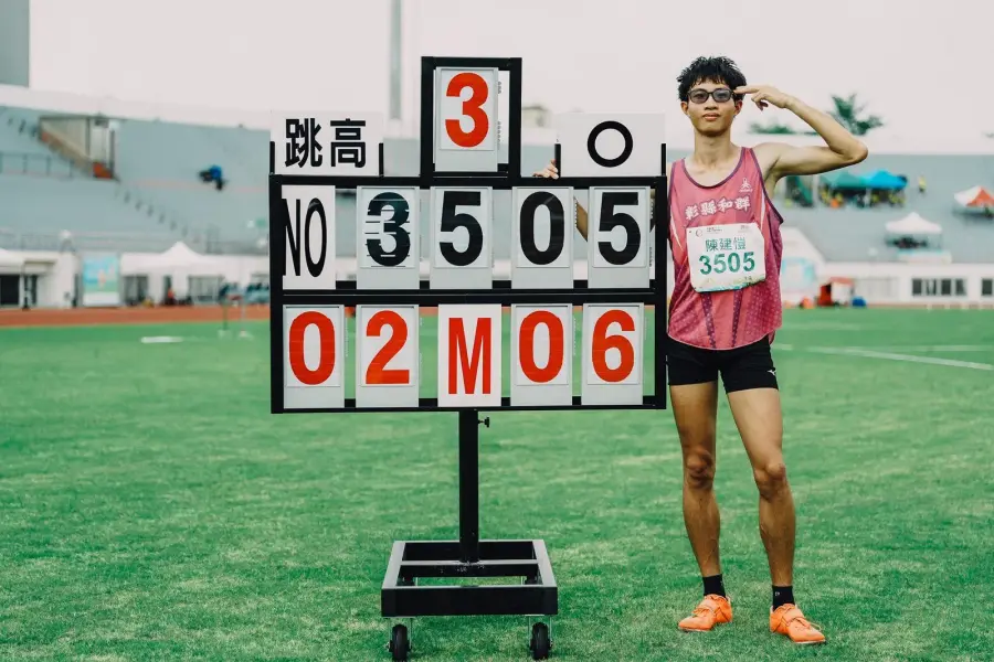 台灣少年跳高選手在田徑場上以背越式動作越過橫桿，後方可見落墊與模糊的觀眾席。