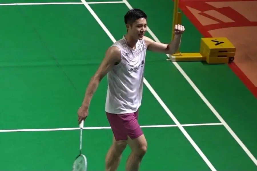 一名台灣男子羽球選手在室內球場跨步壓低身體回擊羽球。