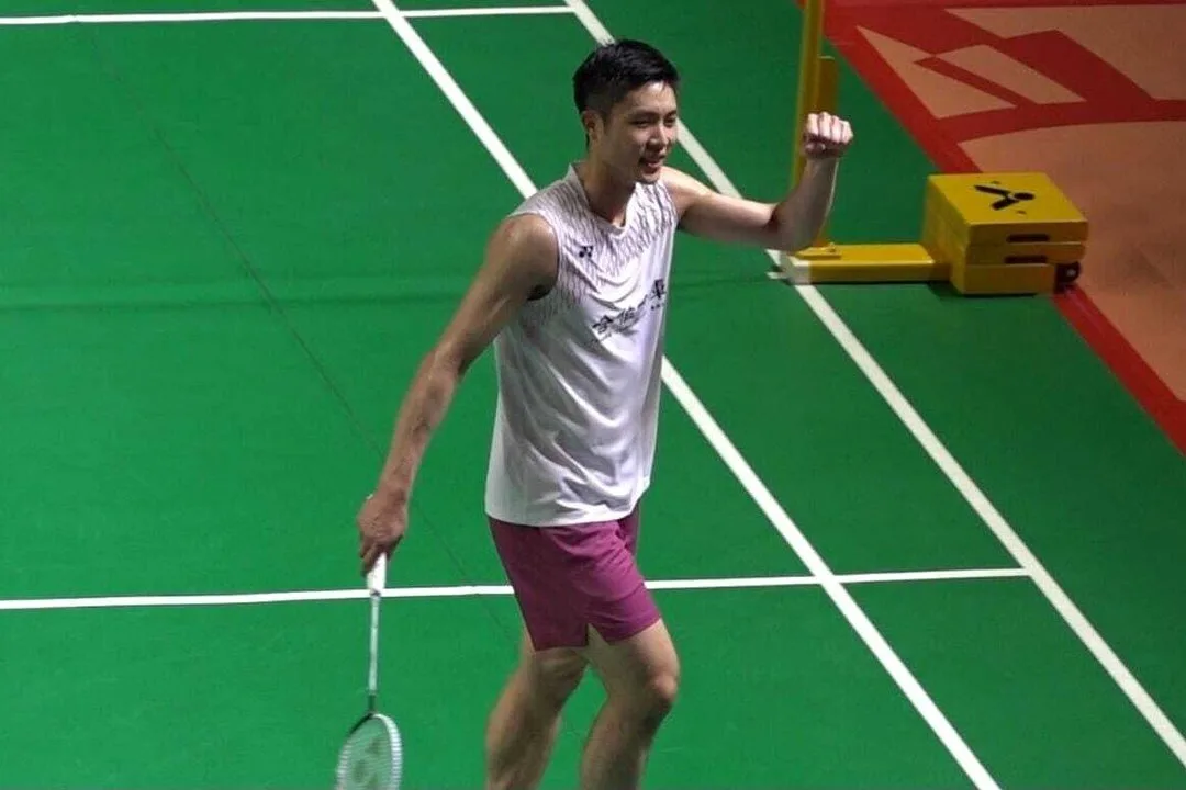 一名台灣男子羽球選手在室內球場跨步壓低身體回擊羽球。