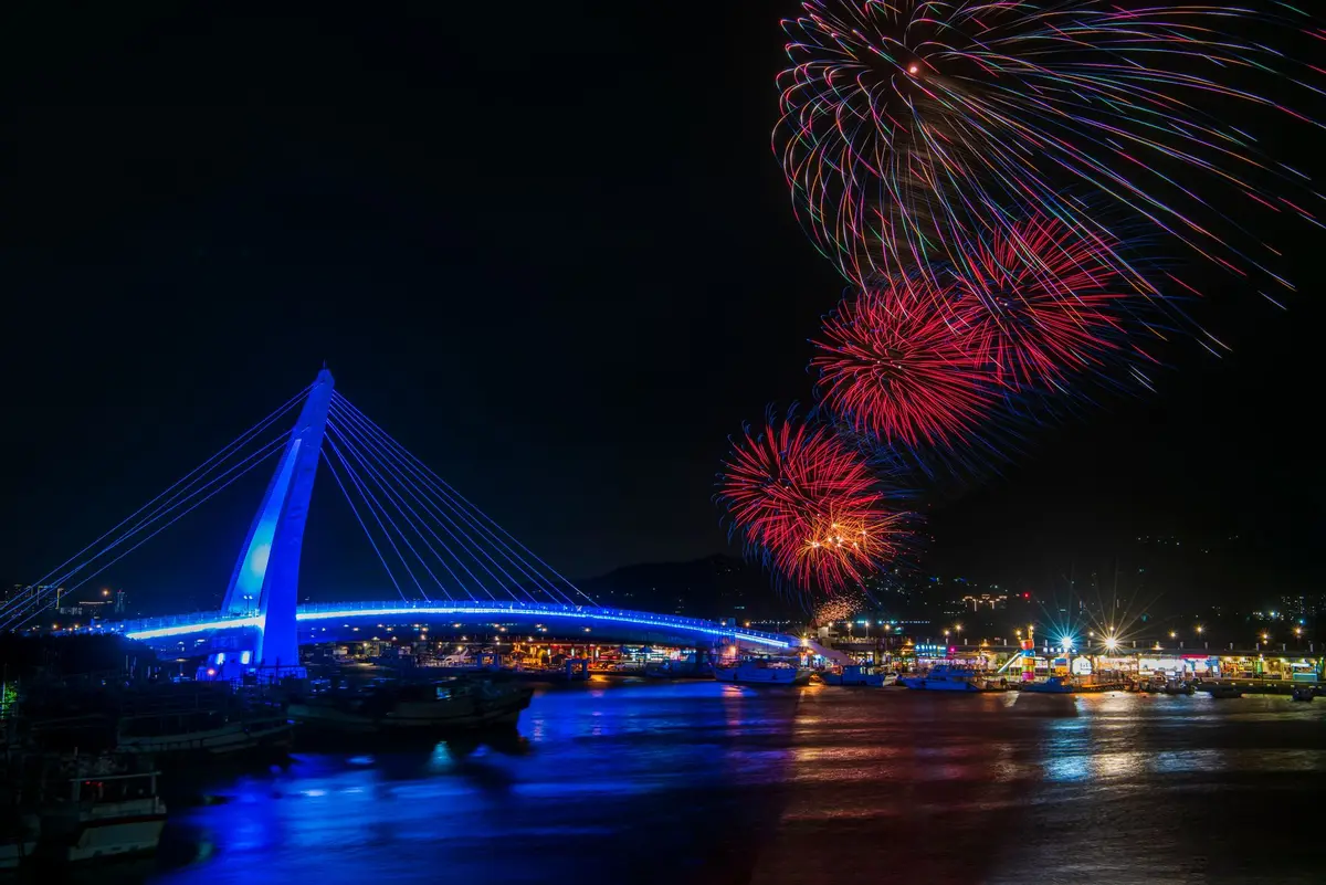 夜間港口與亮燈橋樑上空綻放煙火，象徵海港節慶活動氛圍（示意圖）