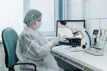 身穿防護裝備的女性科學家在實驗室使用顯微鏡檢視樣本