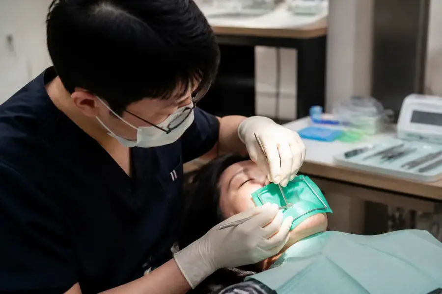 牙科診間進行根管治療，病人張口、放置橡皮障，牙醫師手持器械操作