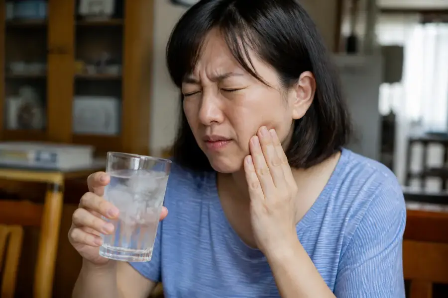 一個人喝冰飲時因牙齒敏感而皺眉、伸手摀住臉頰