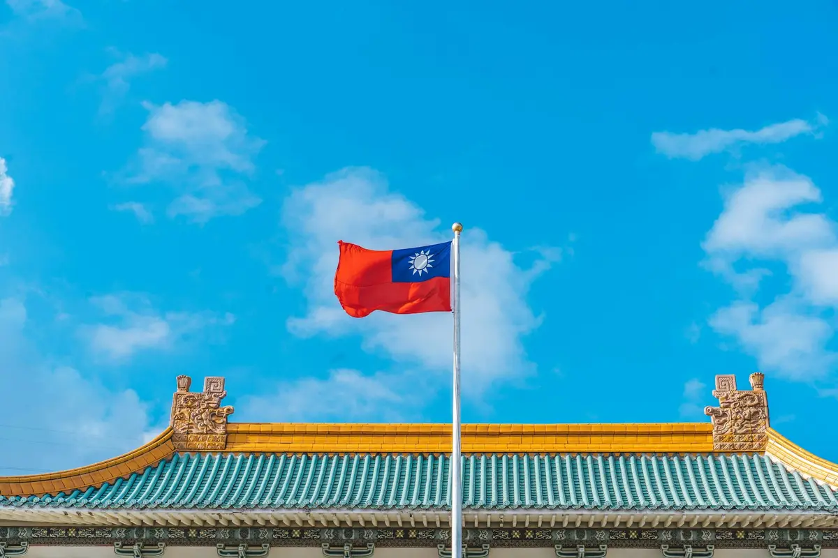台灣傳統建築屋頂上飄揚的中華民國國旗，藍天白雲為背景（示意圖）
