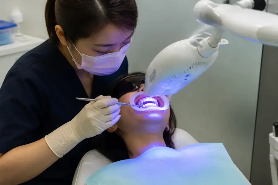 牙科診間進行冷光美白療程，病人戴著開口器、藍光美白儀器對準牙齒