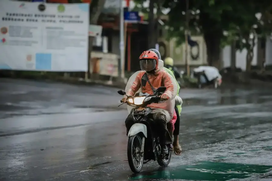 雨後城市道路上一輛機車載著乘客行駛，路面濕滑反光