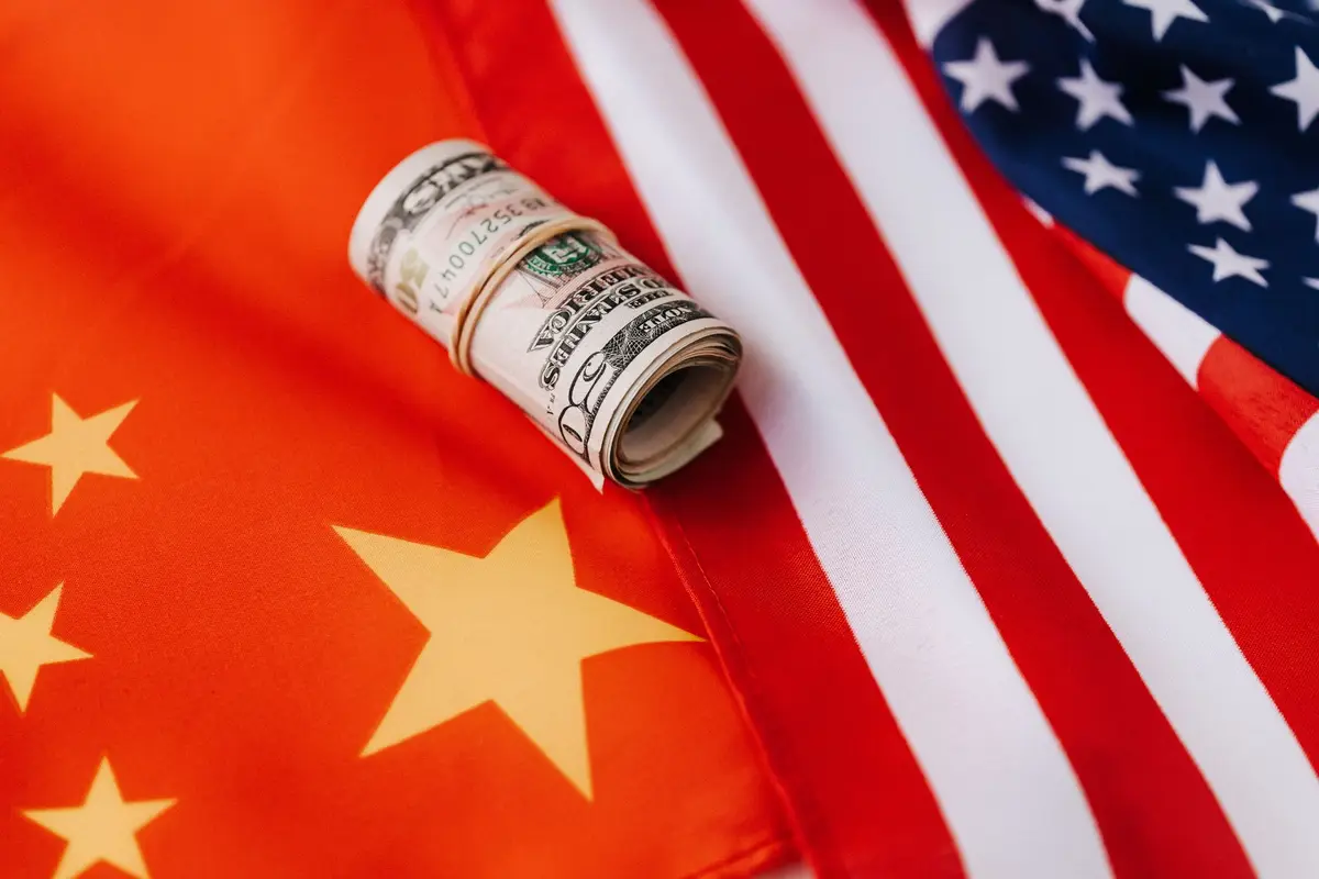 美國與中國國旗並列，美元紙鈔放在兩國旗幟上，象徵美中貿易談判