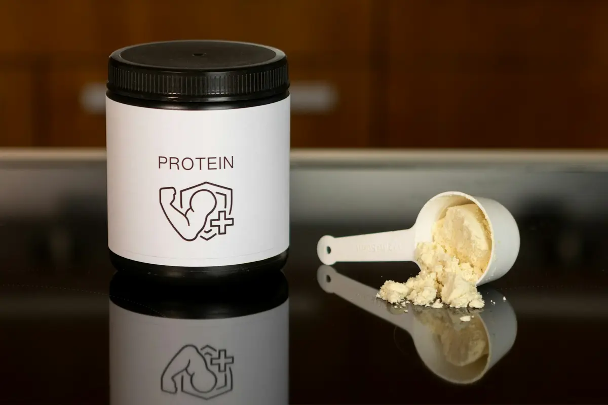A tub of whey protein powder, a white scoop, a shaker bottle and milk on a table (illustrative image)
