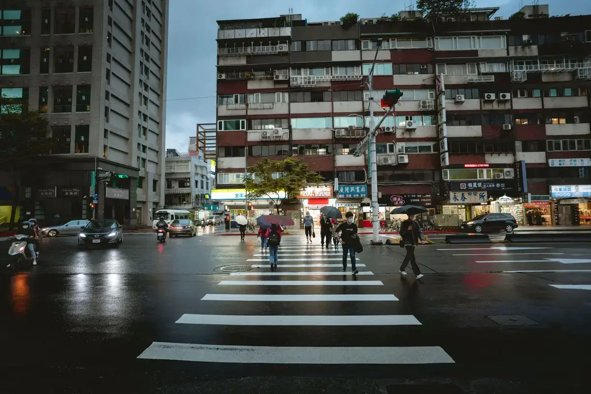 雨天台灣市區路口與行人，呈現颱風豪雨期間查詢停班停課公告的情境