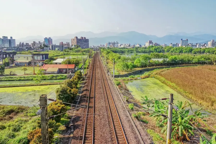 台灣鐵路穿越農田與城市，遠方是山脈，象徵高鐵延伸宜蘭連結交通與生活圈