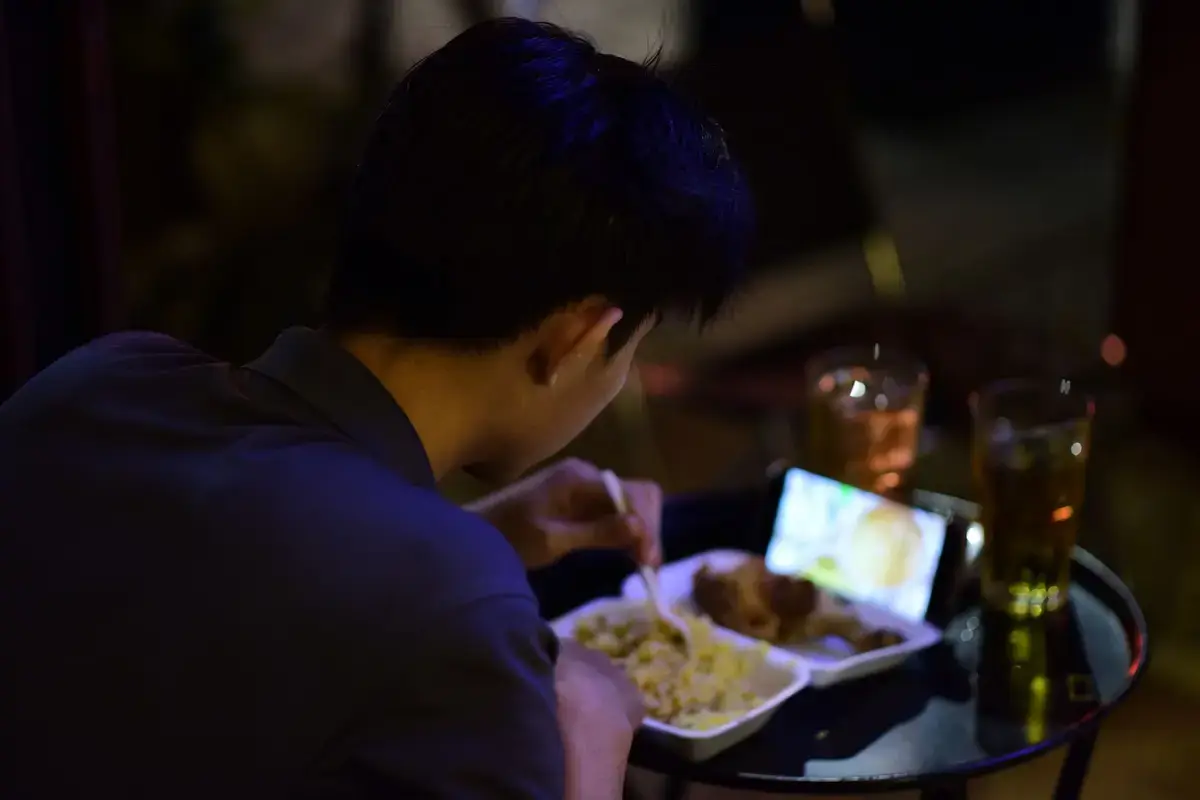 餐桌前觀看食物影片的用餐場景，手機畫面呈現影片觀看情境（示意圖）