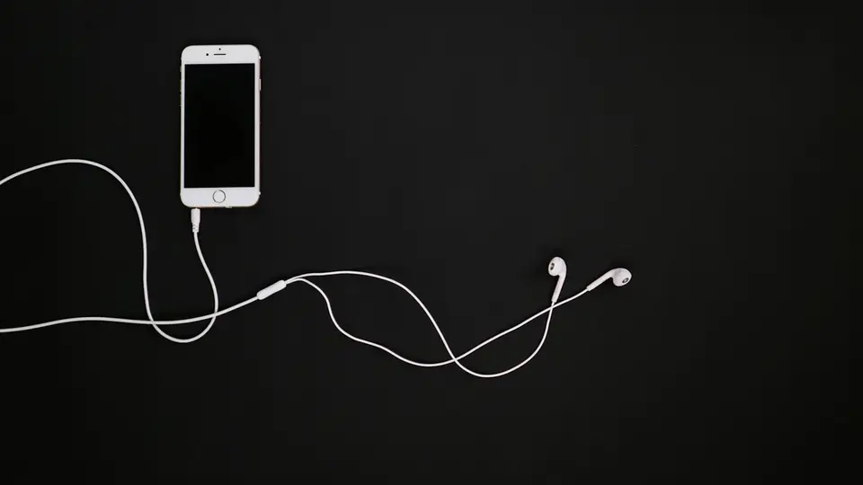 桌上的手機與耳機，螢幕顯示音樂串流 App