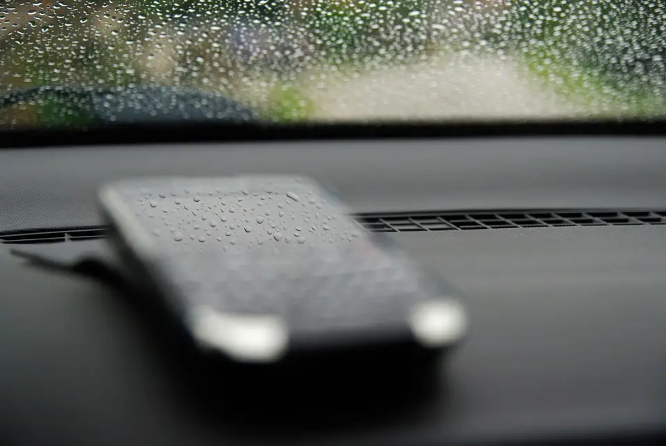 雨天車內的手機與擋風玻璃水滴，象徵出門前查詢 8 月 24 日停班停課官方公告