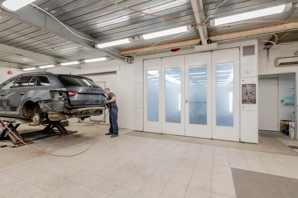 汽車維修廠內技師正在處理後車身鈑件，旁邊是噴漆工作區