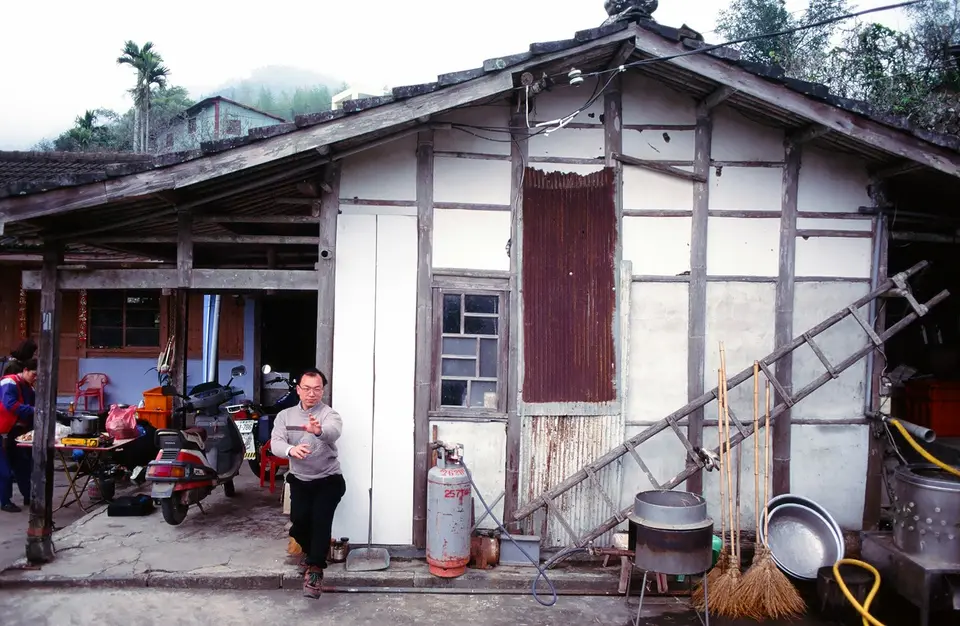 住宅建物外牆與屋頂受損，周邊可見清理工具與生活用品