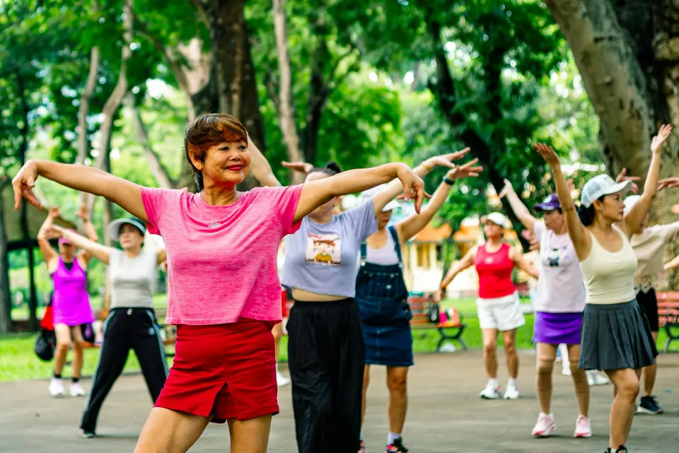 一群中高齡女性在公園戶外空間跟著帶領者做伸展體操，面帶微笑、精神飽滿