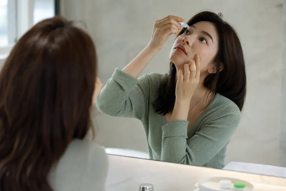 一個人對著鏡子點人工淚液,準備取下隱形眼鏡