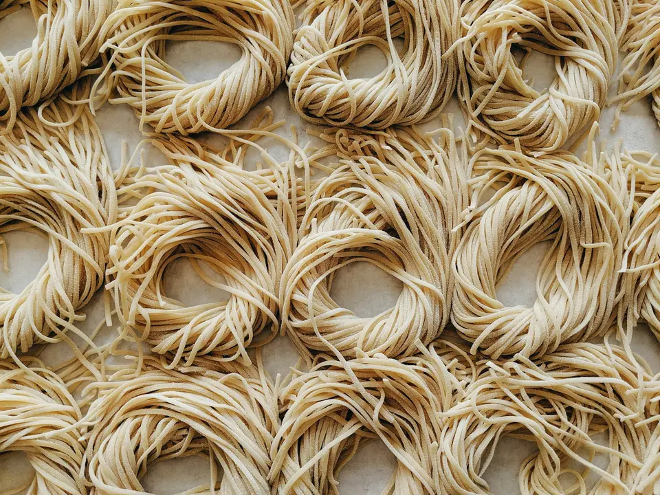 食品製程中以熱水與網籃處理麵條的近距離畫面，呈現麵體加熱與復水概念（示意圖）