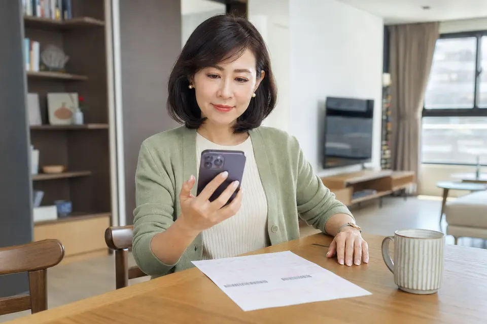台灣中年女性在家用手機查詢地價稅，桌面放著地價稅繳款書，呈現數位繳稅管道