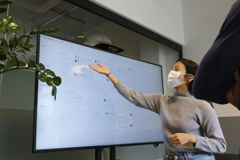 辦公室大螢幕播放影片，前方有筆電與簡報資料