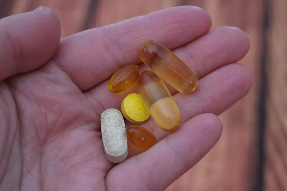 手掌托著多種不同形狀的保健食品錠劑和膠囊，背景為深紅色上衣