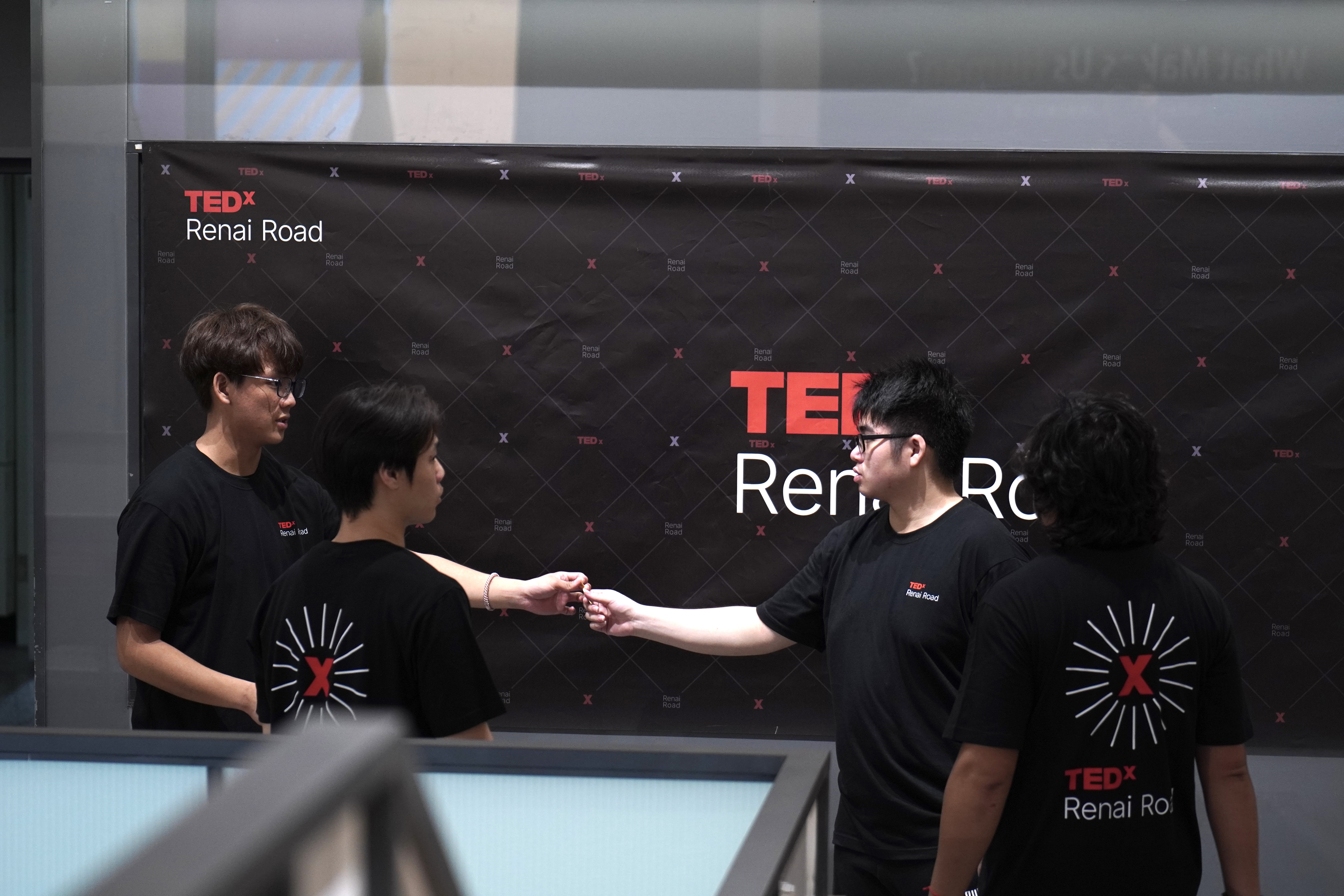 TEDxRenaiRoad志工在活動海報前進行工作交接，呈現現場協作與任務銜接