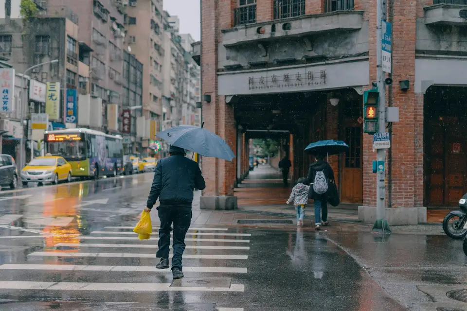 雨天城市街道上有車輛與行人通行，呈現道路修補前的用路情境
