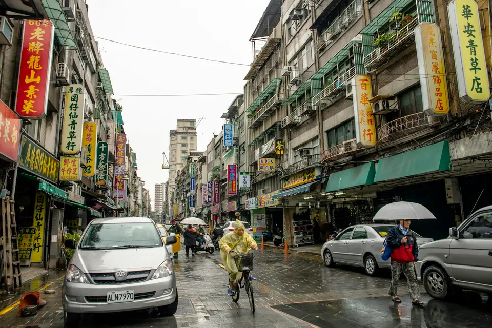 雨天台灣街道上有機車與汽車通行，路面反光呈現濕滑路況