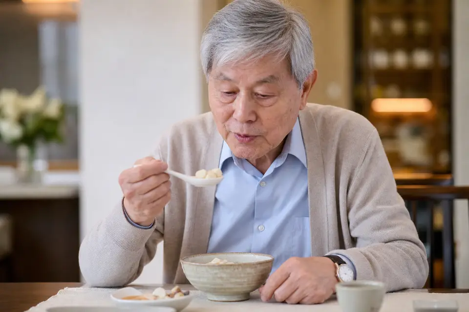 長者以湯匙小口進食湯圓，桌上放著溫熱餐碗，呈現吞嚥安全提醒
