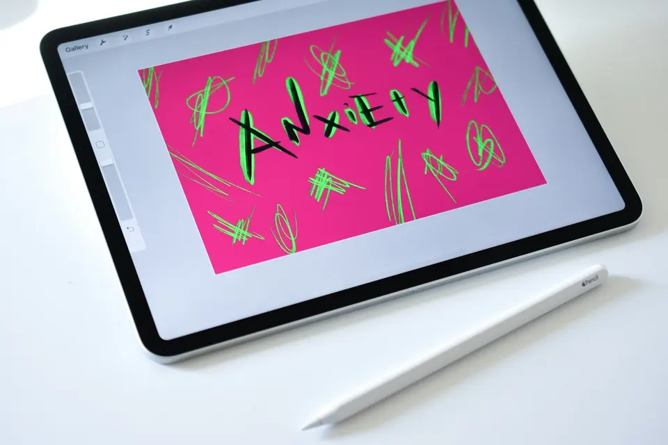 iPad 螢幕上以黑色粗筆手寫「ANXiETy」字樣,周圍佈滿混亂的塗鴉線條,象徵焦慮感受