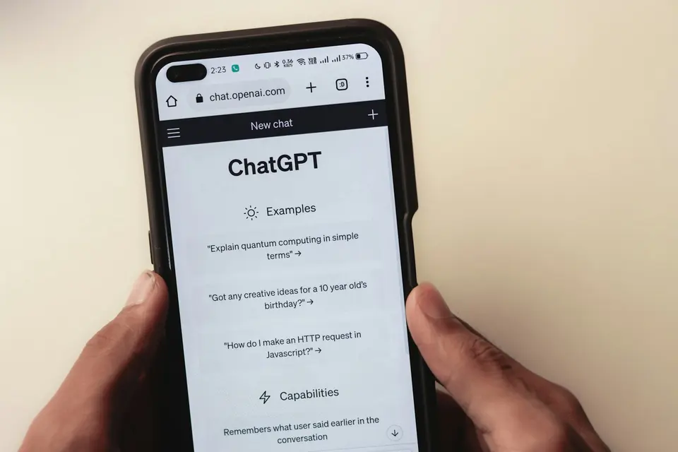 雙手握著顯示 ChatGPT 介面的手機，螢幕上可見對話輸入框與示例提示