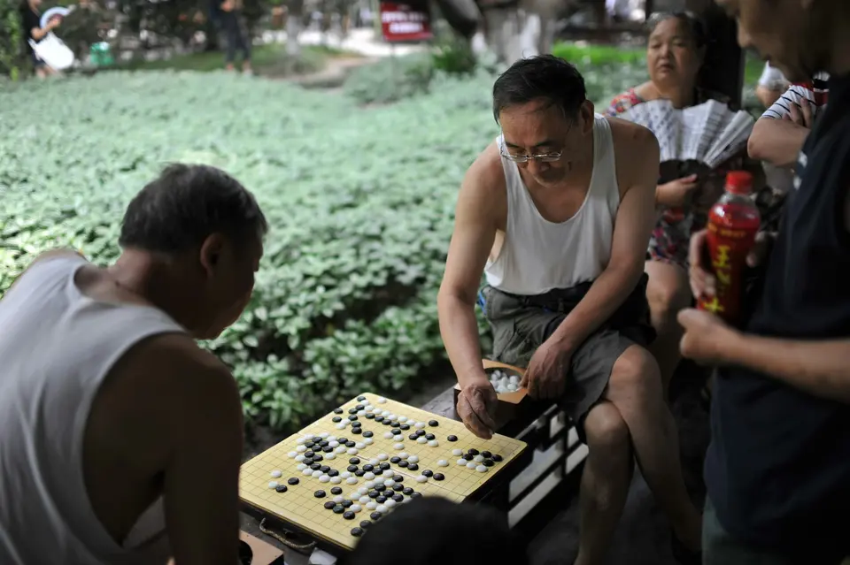 兩名男性在戶外公園對弈圍棋，神情專注，旁有觀棋者