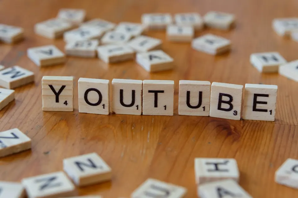 Scrabble 字母積木在木桌上拼出 YOUTUBE 字樣，周圍散落其他字母積木