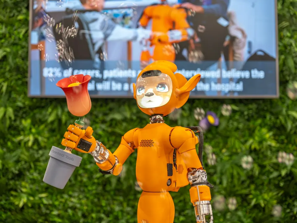 橘色人形醫療機器人站在展示牌前，牌上顯示醫療 AI 相關統計數字，背景為植物牆