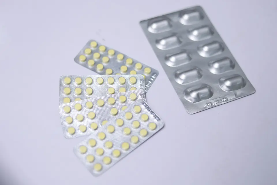 多片鋁箔包裝的黃色藥錠與銀色膠囊散放在白色背景上