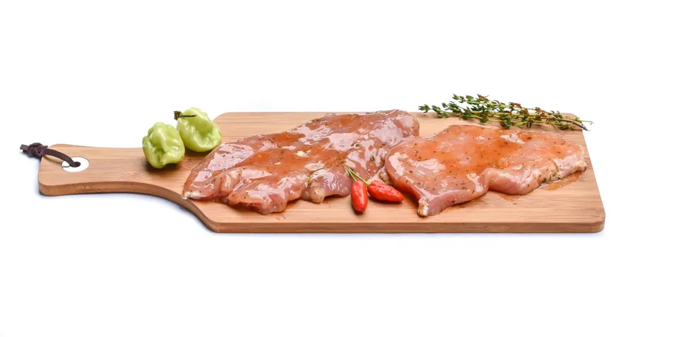 木製砧板上擺放的生雞肉切片，旁邊有青椒、辣椒和香草